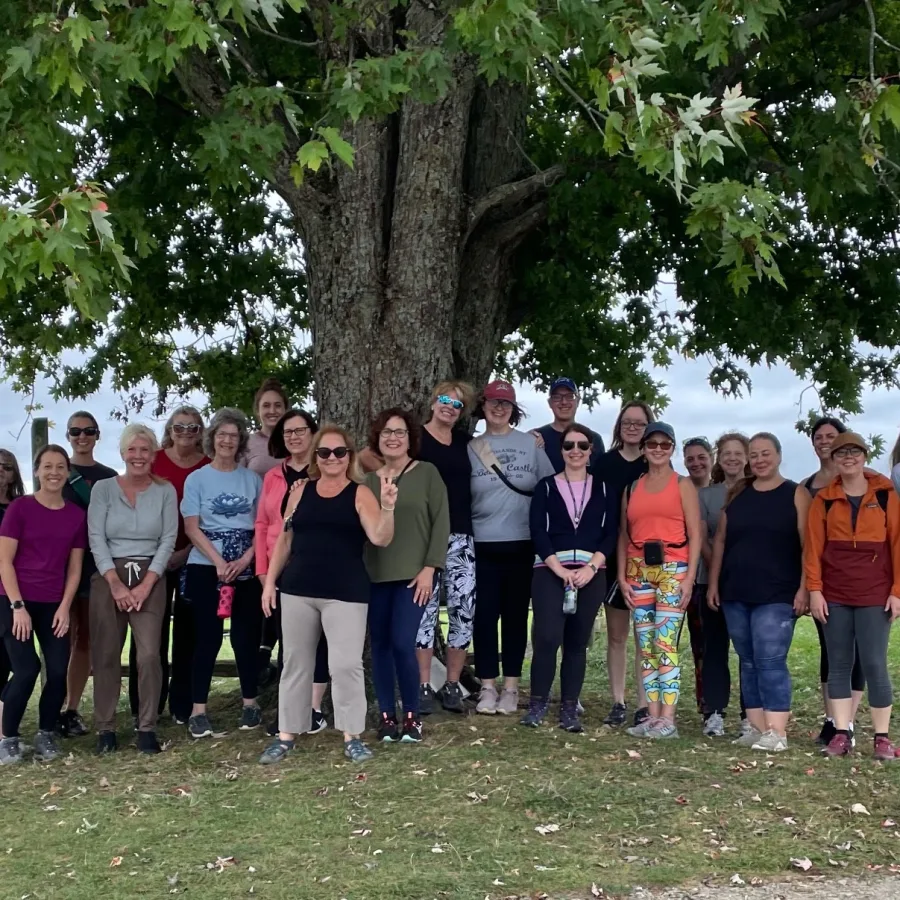 A large group of students smiling together under a maple tree after an outdoor class